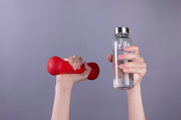 Girl 's hand holding red dumbbell and bottle of water on grey background. concept.  Sport and healthy lifestyle concept with Copy space.