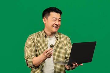 Aufkleber - Happy mature asian man holding golden bitcoin and laptop, earning cryptocurrency, standing over green background