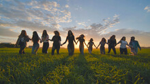 A Group Of Girls Walk Towards The Sun At Sunset Holding Hands.