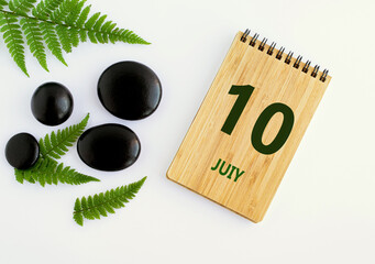 July 10. 10th day of the month, calendar date. Notepad, black SPA stones, green leaves. Summer month, day of the year concep