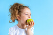 © Елена Якимова - cute child smiling bites apple. nutrition for caries prevention. portrait of little girl with fruit on blue background. kid eating healthy food, snack.  teeth, dental health, smile. children dentistry