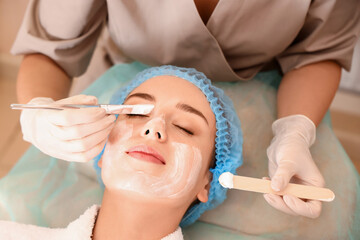 Poster - Cosmetologist applying mask onto young woman's face in beauty salon