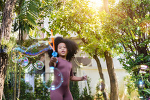 Happy African American Girl Blowing Soap Bubbles And Having Fun At Home Garden