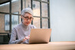 Mature asian business woman wears glasses using laptop computer sit at workplace desk. Happy senior older employee 50s businesswoman.