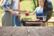 © New Africa - Empty wooden table and blurred view of family having barbecue with modern grill outdoors