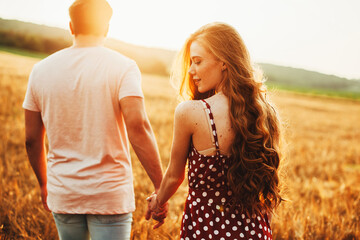 Lovers walking hand in hand in autumn field. Back view. Love, dating. Wheat field.