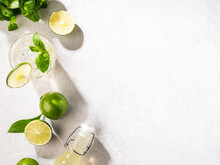Flat-lay Of Mojito Cocktail With Lime, Fresh Mint And Ice, Bottle With Mojito On White Texture Background Close Up. Summer Refreshment Citrus Drink. Top View And Copy Space