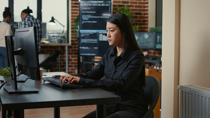 Wall Mural - system engineer focused on writing code sitting at desk in software development office while team of