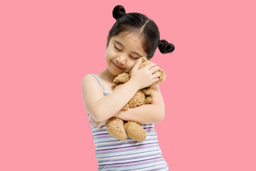 Wall Mural - Asian cute little Asian child girl hugging teddy bear isolated on pink background.