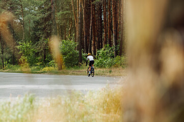 Male cyclist in sportswear trains in the woods outside the city on an asphalt road.