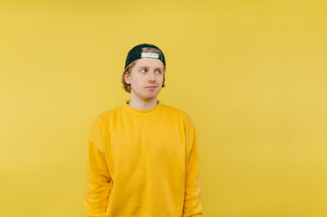 Wall Mural - Handsome young man in a cap and yellow sweatshirt stands on a colored background and looks away.