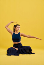 Concentrated Female Performing Yoga Asana In Studio. Front View Of Sporty Woman Sitting In Lotus Pose With Raised Bent Hand Over Head And Outstretched Fingers While Exercising. Concept Of Yoga Asana.