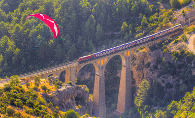 Wall Mural - Paraglider flies in the sky - Aerial view of a train moving on the Varda railway bridge