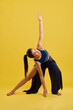 © serhiibobyk - Young girl in slits pants doing triangle pose, looking up in roomy studio. Front view of woman with ponytail practicing trikonasana, isolated on orange studio background, copy space. Concept of yoga.