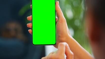 Woman at home using smartphone with green mock-up screen in vertical mode. Girl browsing Internet, watching content, videos