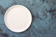 Empty white plate on blue concrete background. Top view, with copy space