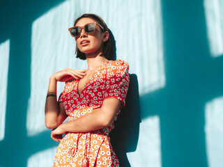 Young beautiful smiling female in trendy summer red dress. Sexy carefree woman posing near blue wall in studio. Positive model having fun. Cheerful and happy. At sunny day. Shadow from window