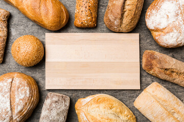 Wall Mural - Minimalist wooden cutting board blank mockup on background of Types of homemade bread. Different kinds of fresh bread as background, top view with space for your text or design