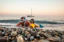 Young Caucasian Man With His Son 4 Years Old Swim Near Shore In Masks With Snorkels At Sunset, In Background Is A Yacht.