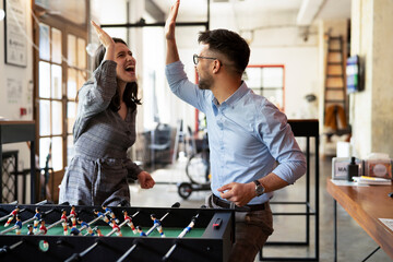 Colleagues having fun at work. Businessman and businesswoman playing table soccer