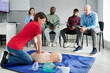 © pressmaster - Medical instructor showing CPR on training mannequin on floor to people who sitting on chairs and watching during lesson