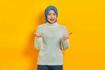 Surprised beautiful Asian woman in white sweater looking at camera with open mouth and raising his palms up isolated over yellow background