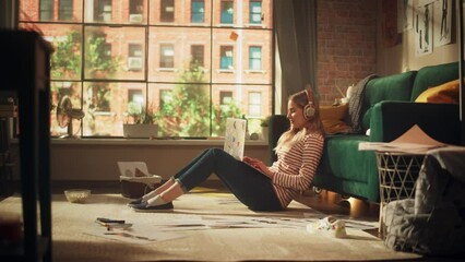 Poster - Young Pretty Woman with Blond Hair Wearing Headphones while Working from Home on Laptop Computer in Stylish Loft Apartment. Creative Female Sitting in Relaxed Pose and Checking Social Media