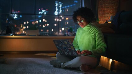 Poster - Beautiful Authentic Latina Female Sitting at the Floor in a Cozy Living Room and Using Laptop Computer at Home. She's Browsing the Internet and Checking Videos on Social Networks