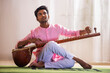 © IndiaPix - Young male musician tuning his sitar while sitting in living room