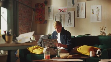Poster - Handsome Caucasian Man Sits at the Sofa with Laptop, Working from Home in Stylish Loft Office. Creative Male Stands and Going to the Table. Urban City View from Big Window