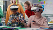 Teenagers looking at classmates in vr headset and joystick playing game in classroom