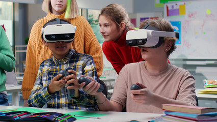 teenagers looking at classmates in vr headset and joystick playing game in classroom