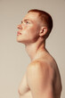 © Lustre Art Group  - Side view portrait of attractive young red-haired man with muscular body shape posing isolated over beige studio background