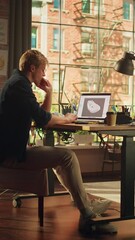 Poster - Blonde Male Artist Pondering in front of Laptop with 3D Model of Sneakers on Screen and Examining Custom Made Shoe at his Loft Apartments. Footwear Customisation and Handmade Concept. Vertical Shot