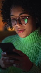 Aufkleber - Vertical Portrait of Black Female with Curly Hair Sitting at Home while Using Smartphone. Positive Woman Browsing Web, Checking Social Media and Chatting with Friends. Slow Motion