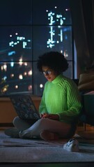 Poster - Black Female Student in Cozy Green Jumper Working at her Laptop During the Evening. Smart Woman Pondering, Smiling, Answering Emails. Girl Study Late at Night. Vertical Shot