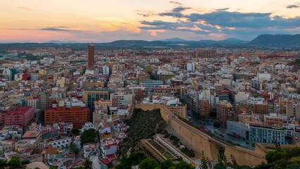 Wall Mural - Alicante, Spain. Aerial view of Alicante, Spain in the evening. It is a popular summer resort of Costa Blanca. Time-lapse, illumination at sunset. Mountains at the background, zoom in