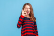 © khosrork - Portrait of woman wearing striped casual style sweater standing showing ok sign and winking to camera, approval sign, agreeing with suggestion. Indoor studio shot isolated on blue background.