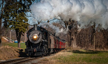 An Antique Steam Passenger Train Approaching On A Single Track Blowing Smoke On A Sunny Day