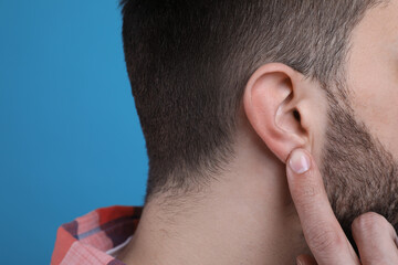 Man pointing at his ear on light blue background, closeup