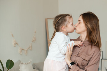 a little girl kisses her mother at home in a modern bright bedroom. the concept of parenthood, love 