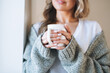 Close up portrait of Young beautiful woman forty year with blonde long curly hair in cozy knitted grey sweater with cup of tea in hands in bright interior at the home