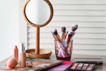 Canvas Print - Holder with makeup brushes, cosmetic products and magazines on table in room