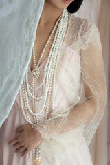 A woman's wearing a pink vintage dress with a lace shawl, and pearls against a soft fabric background