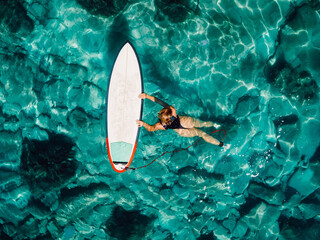 Wall Mural - Surf girl floating with surfboard in transparent turquoise ocean. Aerial view