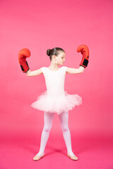 Proud classical dancer child wearing boxing gloves. Little ballet dancer girl showing biceps isolated on vivid pink background. Female stereotype concept.