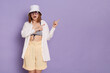 © sementsova321 - Horizontal shot of amazed Caucasian woman wearing swimsuit, shirt, shorts and panama, pointing finger aside at copy space for promotion, posing isolated over purple background.