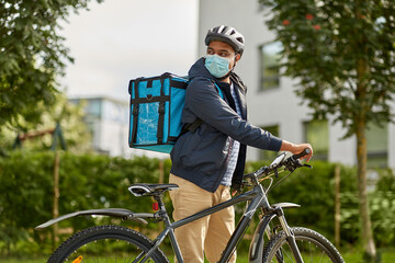 Wall Mural - food shipping, health and people concept - delivery man in bike helmet and protective medical mask with thermal insulated bag and bicycle on city street