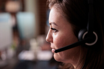 Wall Mural - Female receptionist wearing headphones to work at call center helpdesk, giving telemarketing assistance. Woman working at customer service support to help clients, telephony network. Close up.