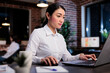 © DC Studio - Attractive developing agency employee sitting at desk in office workspace while analyzing management plan. Marketing company businesswoman reviewing accounting documentation.